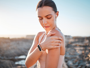 Image showing Beach, fitness and woman holding shoulder pain, standing on rocks at ocean. Nature, sports and arm injury during workout for health and wellness, muscle trauma during stretching exercise in morning.