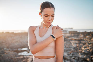 Image showing Beach, fitness and yoga, woman with shoulder pain standing on rocks at ocean. Nature, sports and injury during workout for health and wellness, muscle trauma during stretching exercise in morning.