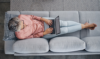 Image showing Senior woman, laptop and sofa above relaxed in the living room checking email, typing or writing at home. Elderly female freelancer or writer relaxing on lounge couch working or reading on computer