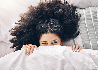 Image showing Bed, wink portrait and black woman in the morning after sleep and rest at home with blanket. Eyes, house and wake up happiness of a young person hiding face under the bedroom covers on a pillow