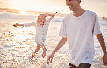 Image showing Couple at beach, splash in water with ocean, travel and freedom outdoor, love and care in relationship with youth. Cafe free at sunset, nature and sea waves with young people on holiday in Hawaii