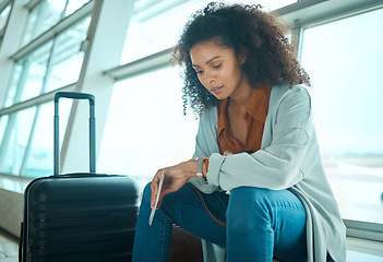 Image showing Airport, black woman and watch time check of a young female at plane terminal with flight delay. Waiting, sitting and person with passport document looking at smartwatch for board and transport info