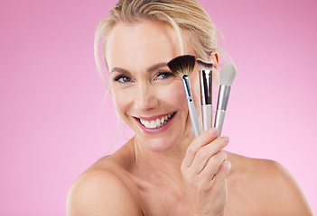 Image showing Portrait, makeup and brushes with a mature woman in studio on a pink background to promote a cosmetic product. Face, happy and cosmetics with an attractive older female posing for beauty treatment