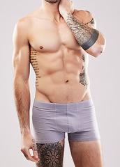 Image showing Fitness, muscle and man body in studio with fitness, exercise and workout aesthetic. Isolated, gray background and studio with a sexy, strong and young male model in underwear with tattoos and abs