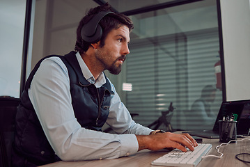 Image showing Headphones, programmer keyboard and man typing, coding or programming online at night. Information technology, computer and male employee or coder working on software while streaming music or radio.