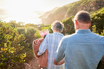 Image showing Picnic, romance and senior couple walking in nature with blanket and flowers for love and valentines day. Mountain path, old man and woman holding hands on walk for romantic valentine date from back.