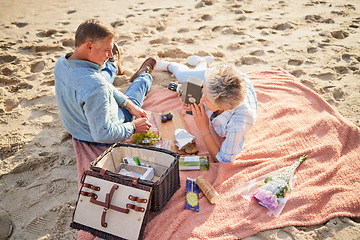 Image showing Senior couple, beach and picnic basket above for romantic getaway, travel or valentines day celebration in nature. Happy elderly man and woman relax by a sandy ocean coast for date, meal or trip