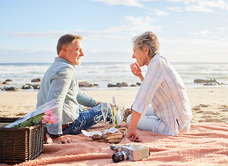 Image showing Senior couple, beach and picnic on blanket for romantic getaway, travel or valentines day celebration in nature. Happy elderly man and woman relax by a sandy ocean coast for date, basket meal or trip