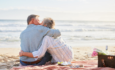 Image showing Senior couple, beach picnic and kiss with hug, romance and happiness in summer for anniversary celebration. Elderly man, old woman and basket for food, wine and outdoor for sunshine, waves and love