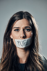 Image showing Woman, face and tape on mouth for fuel prices, ecumenic struggle or financial crisis against gray studio background. Portrait of female activist with covered lips in silence, speech or voice message