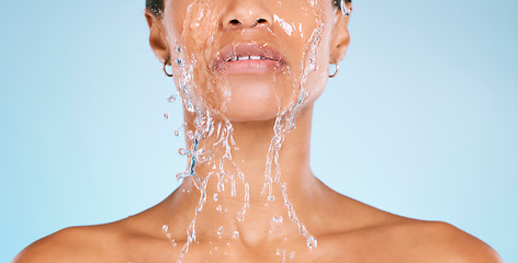 Image showing Face, water and cleaning with a black woman in studio on a blue background for hygiene or hydration. Splash, shower and bathroom with a young female washing her body for natural skincare or wellness