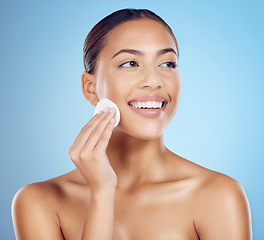 Image showing Skincare, beauty and woman with cotton pad on face, smile and makeup or dirt removal with luxury skin product in studio. Dermatology, cosmetics and facial for happy model isolated on blue background.