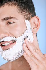 Image showing Shaving, foam and smile on face, man with hand on beard, product placement and mock up in studio. Shave cream facial, luxury hair and skincare for male model with smile, isolated on blue background.