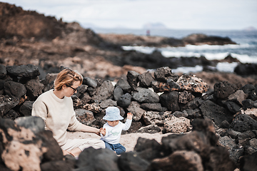 Image showing Mother playing his infant baby boy son on sandy beach enjoying summer vacationson on Lanzarote island, Spain. Family travel and vacations concept.