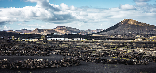 Image showing Traditional white houses in black volcanic landscape of La Geria wine growing region with view of Timanfaya National Park in Lanzarote. Touristic attraction in Lanzarote island, Canary Islands, Spain.