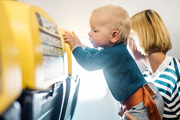 Image showing Mom and child flying by plane. Mother holding and playing with her infant baby boy child in her lap during economy comercial flight. Concept photo of air travel with baby. Real people.