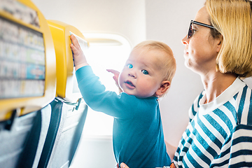 Image showing Mom and child flying by plane. Mother holding and playing with her infant baby boy child in her lap during economy comercial flight. Concept photo of air travel with baby. Real people.