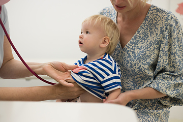 Image showing Infant baby boy child being examined by his pediatrician doctor during a standard medical checkup in presence and comfort of his mother. National public health and childs care care koncept.