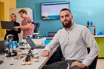 Image showing A man sitting in a robotics laboratory while his colleagues in the background test new, cutting edge robotic inventions.