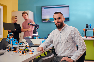 Image showing A man sitting in a robotics laboratory while his colleagues in the background test new, cutting edge robotic inventions.