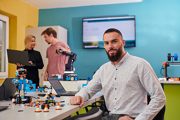 Image showing A man sitting in a robotics laboratory while his colleagues in the background test new, cutting edge robotic inventions.