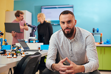 Image showing A man sitting in a robotics laboratory while his colleagues in the background test new, cutting edge robotic inventions.