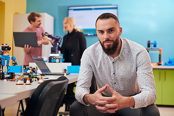 Image showing A man sitting in a robotics laboratory while his colleagues in the background test new, cutting edge robotic inventions.