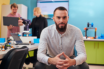 Image showing A man sitting in a robotics laboratory while his colleagues in the background test new, cutting edge robotic inventions.