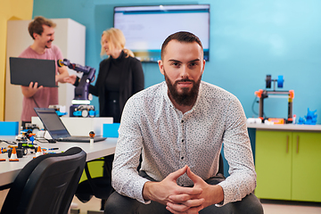 Image showing A man sitting in a robotics laboratory while his colleagues in the background test new, cutting edge robotic inventions.