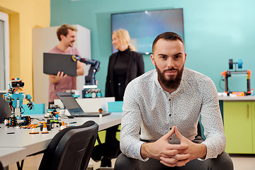 Image showing A man sitting in a robotics laboratory while his colleagues in the background test new, cutting edge robotic inventions.