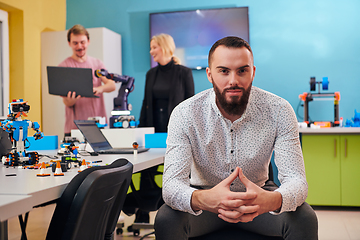 Image showing A man sitting in a robotics laboratory while his colleagues in the background test new, cutting edge robotic inventions.