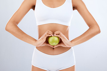 Image showing Digestion, apple and woman stomach with hands in heart shape for nutrition, detox diet and studio background. Fruits, wellness and healthy abdomen body with care, love and lose weight for strong gut