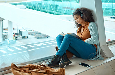 Image showing Airport, travel and black woman reading a book by window waiting for global flight, departure and transport. Immigration, travelling lobby and girl relax with headphones for music, podcast and audio