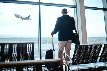 Image showing Airport, suitcase and businessman waiting to board flight by the terminal for corporate work trip. Travel, luggage and professional male traveler watching flying plane by a window in terminus lounge.