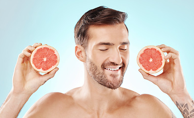 Image showing Man, skincare and grapefruit in studio for health, nutrition and cosmetic wellness by blue background. Happy young model, hands and fruit for vitamin c in natural detox, facial skin glow or aesthetic