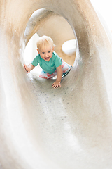 Image showing Child playing on outdoor playground. Toddler plays on school or kindergarten yard. Active kid on stone sculpured slide. Healthy summer activity for children. Little boy climbing outdoors.