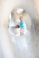 Image showing Child playing on outdoor playground. Toddler plays on school or kindergarten yard. Active kid on stone sculpured slide. Healthy summer activity for children. Little boy climbing outdoors.