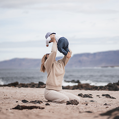 Image showing Mother enjoying winter vacations holding, playing and lifting his infant baby boy son high in the air on sandy beach on Lanzarote island, Spain. Family travel and vacations concept