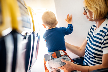 Image showing Mom and child flying by plane. Mother holding and playing with her infant baby boy child in her lap during economy comercial flight. Concept photo of air travel with baby. Real people.