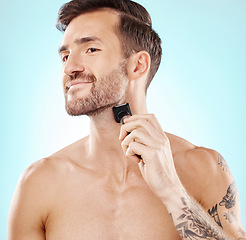 Image showing Man, beard and shaving with trimmer in studio isolated on a blue background for hair removal. Haircare thinking, grooming and male model with electric shaver to shave for hygiene, health or wellness.