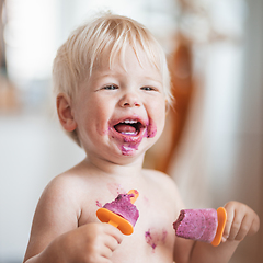 Image showing Happy adorable infant baby boy child smiling while eating two frozen fruit popsicle ice creams in simmer.