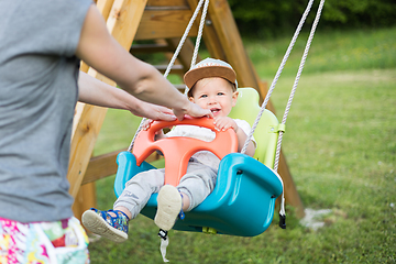 Image showing Mother pushing her infant baby boy child on a swing on playground outdoors.