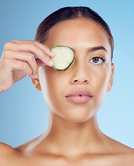 Image showing Cucumber, woman and portrait skincare for face beauty, clean wellness diet and blue studio background. Model, eyes and green fruits cosmetics for detox, facial nutrition or healthy aesthetic benefits