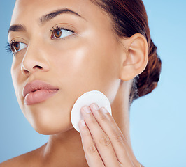 Image showing Skincare, cotton pad and face, woman removing makeup or dirt with luxury skin product in studio. Dermatology, cleaning cosmetics and facial beauty spa treatment for model isolated on blue background.