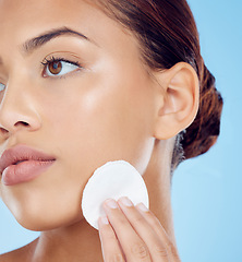 Image showing Beauty, cotton pad and face, woman removing makeup or dirt with luxury skin product in studio. Dermatology, cleaning cosmetics and facial skincare spa treatment for model isolated on blue background.