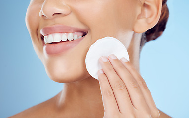 Image showing Skincare, smile and woman with cotton pad on face, removing makeup or dirt removal with luxury skin product in studio. Dermatology, cosmetics and facial for happy model isolated on blue background.