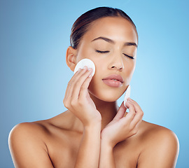 Image showing Skincare, woman with cottonwool on face and eyes closed removing makeup or dirt with luxury skin product in studio. Dermatology, cosmetics and beauty spa facial for model isolated on blue background.