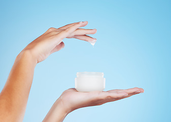 Image showing Skincare, beauty and hands with face cream in studio for a natural, cosmetic or hydration skin routine. Self care, product and closeup of female with spf, sunscreen or facial creme by blue background