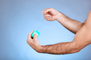 Image showing Floss, dental and man hands with container on studio mockup for teeth, mouth cleaning and marketing. Closeup of flossing product, thread and blue background for tooth cosmetics, mock up and backdrop