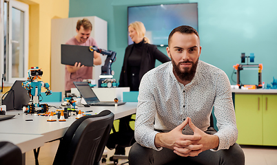 Image showing A man sitting in a robotics laboratory while his colleagues in the background test new, cutting edge robotic inventions.